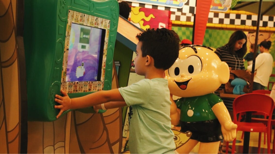 Garoto se diverte em brinquedo interativo "observado" pelo Cebolinha | Foto:  Carla Falcão